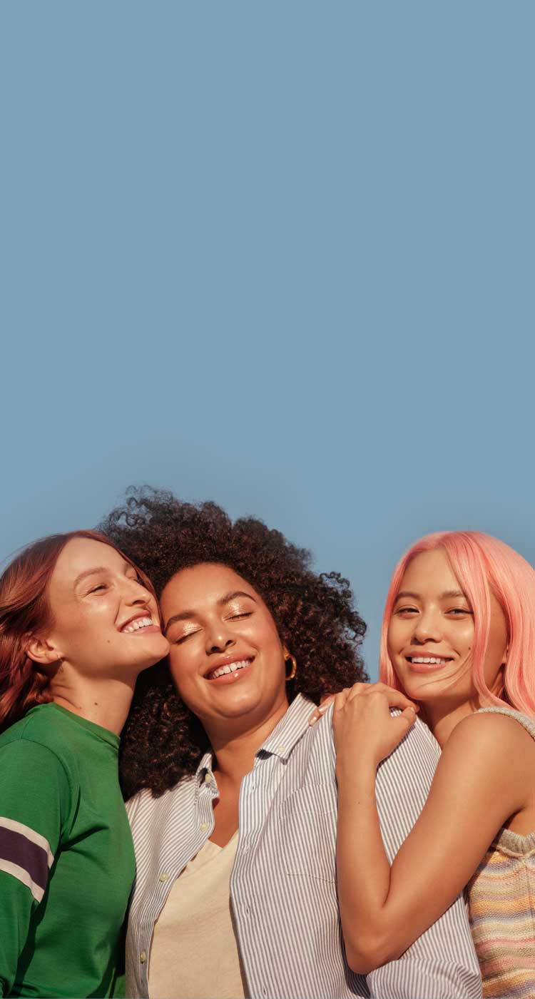 Three women with diverse hair types standing closely together and smiling in front of a blue background