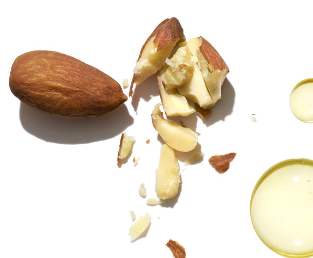 Crushed almonds beside two yellow oil drops on a white background. 