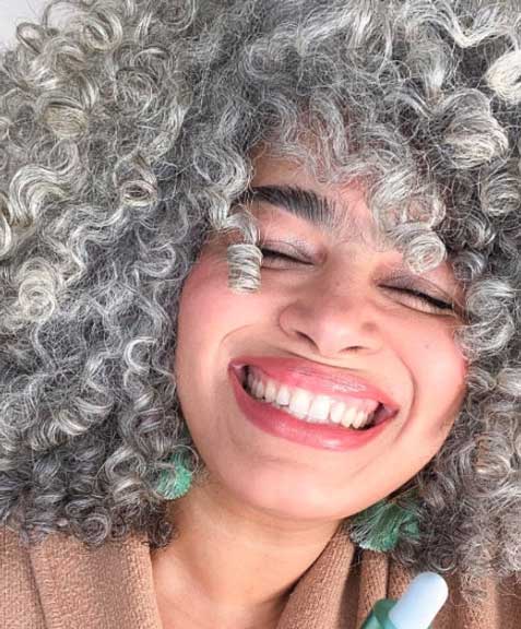 A woman with grey, very curly hair smiling with her eyes closed. 